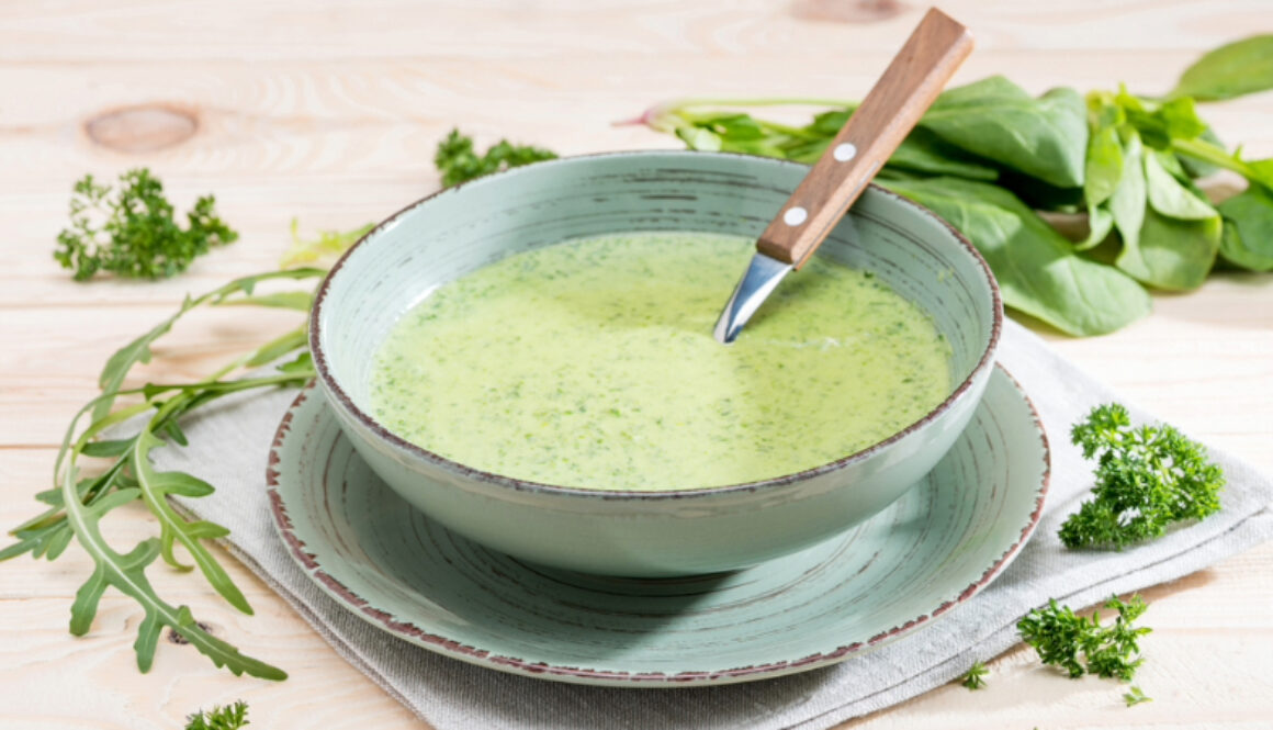 A bowl of green soup with a knife in it.