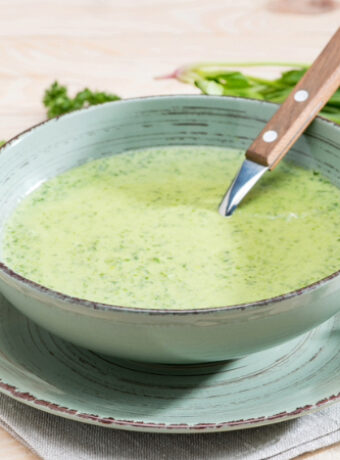 A bowl of green soup with a knife in it.