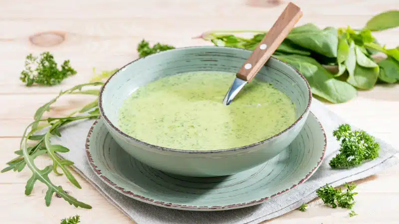 A bowl of green soup with a knife in it.