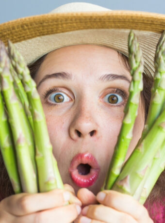 A woman holding asparagus up to her face.