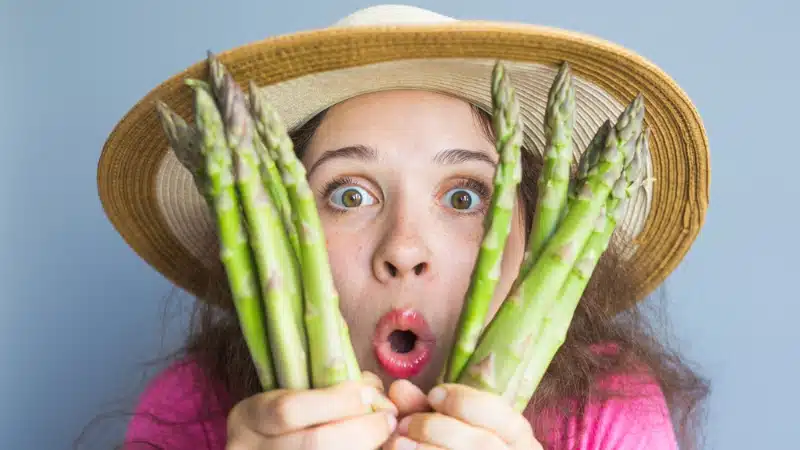 A woman holding asparagus up to her face.