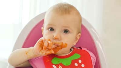 A baby in a pink chair eating food