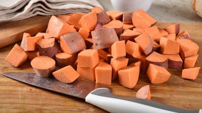 A cutting board with cut up sweet potatoes on it.