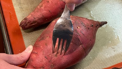 A person holding a fork over an unpeeled sweet potato.