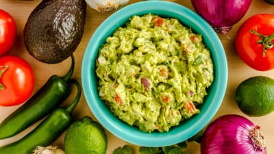 A bowl of guacamole surrounded by other ingredients.