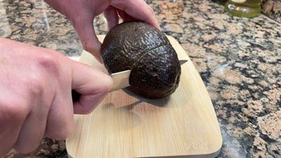 A person slicing an avocado on top of a wooden board.