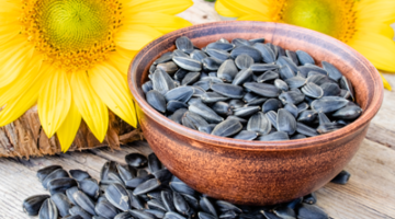 A bowl of sunflower seeds sitting on top of some flowers.