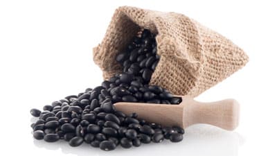 A wooden scoop filled with black beans next to burlap.