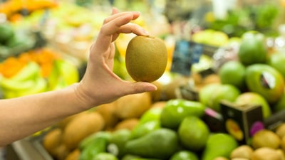 A person holding an apple in front of some other fruit.