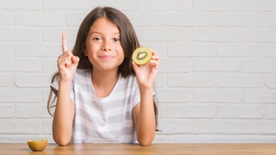 A girl holding up one finger while sitting at the table.
