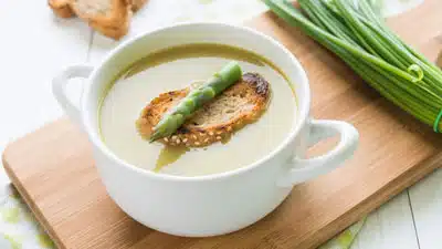 A bowl of soup with bread and green beans.