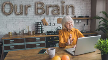Large text made out of chia seeds reads Our Brain while a senior woman works on her laptop looking focused and cheerful.