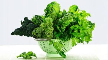 A green bowl filled with leafy greens on top of a table.