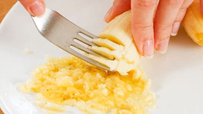 A banana is mashed with a fork.