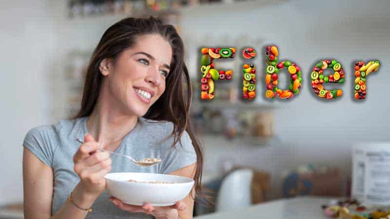 A young woman enjoys a bowl of oats as we see the word Fiber written with a variety of fruits to represent top sources of fiber.